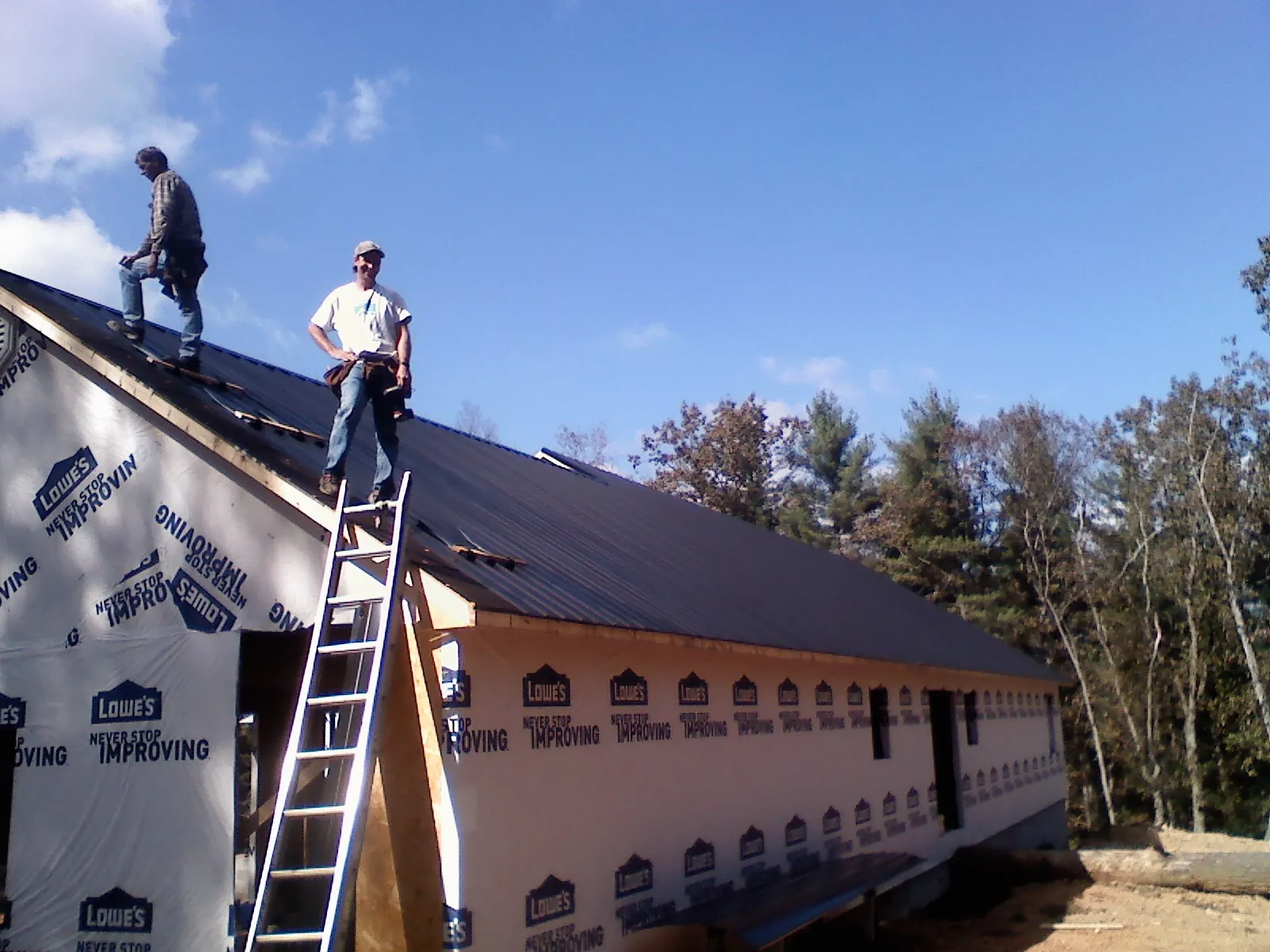 Two roofers standing on a long dark metal roof over a wrapped building in Richland
