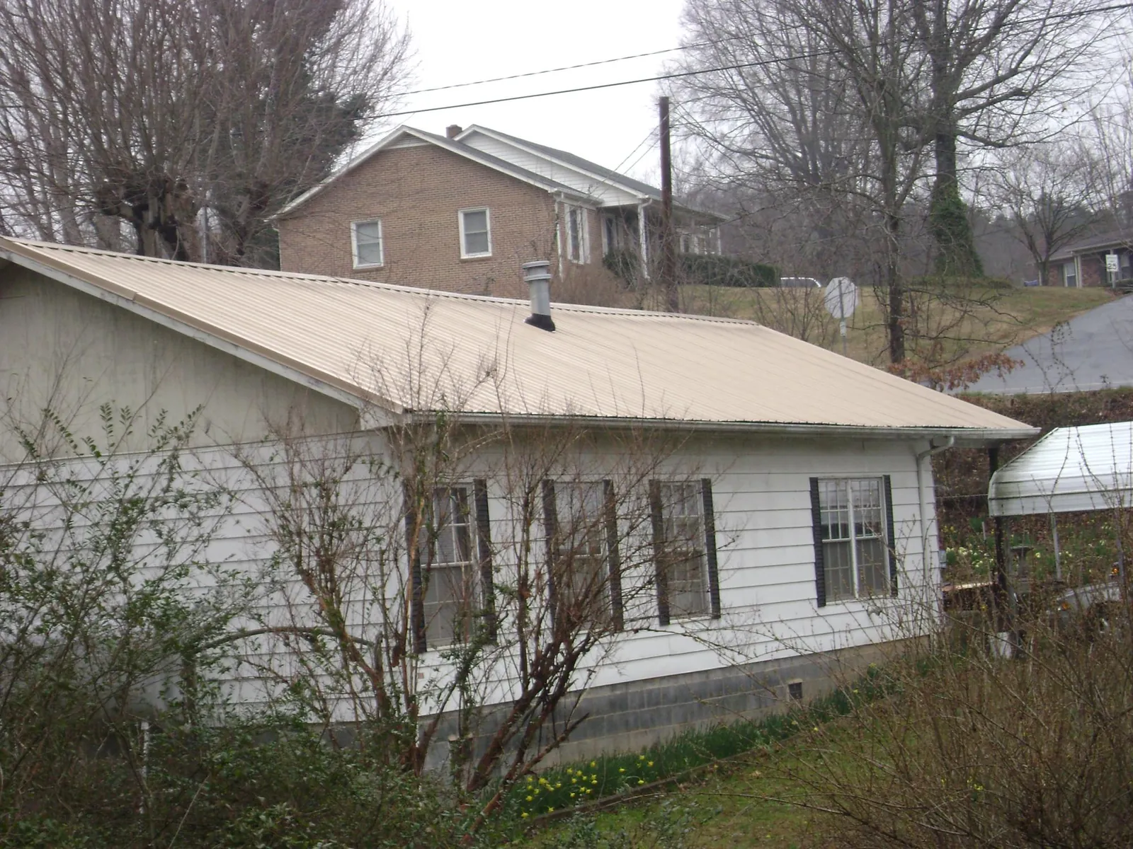 Tan metal roof on a white sided house set into a hillside — Commercial Roofing by Roofing Brothers in Richland
